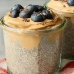 Peanut butter chia pudding in a clear jar with fresh berries and cacao nibs on top