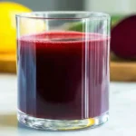 A glass of healthy beet lemonade next to fresh beets and lemons.