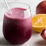 Glass of fresh pomegranate and beet juice with raw ingredients on a wooden table