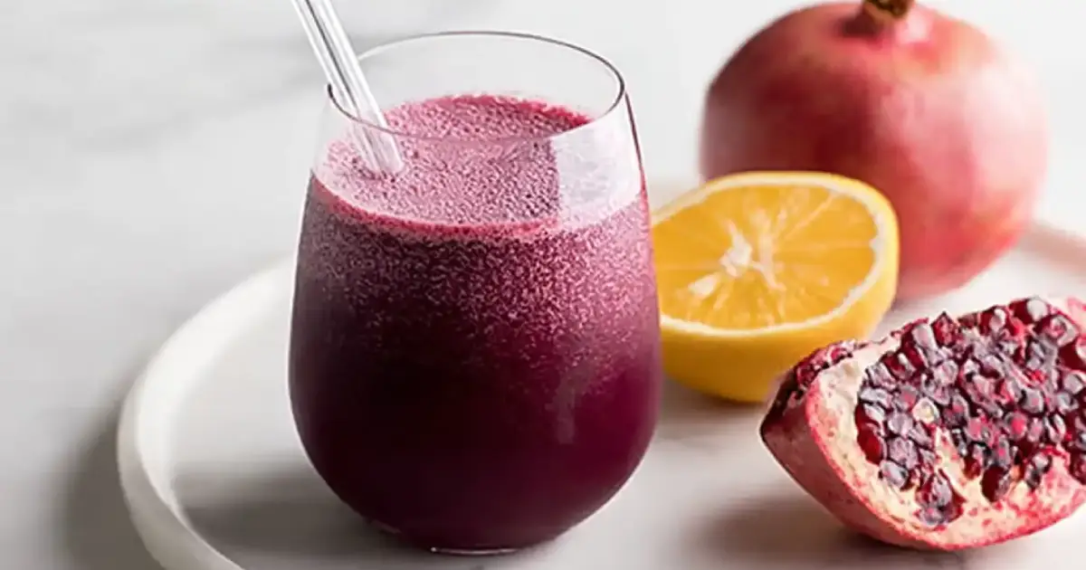 Glass of fresh pomegranate and beet juice with raw ingredients on a wooden table